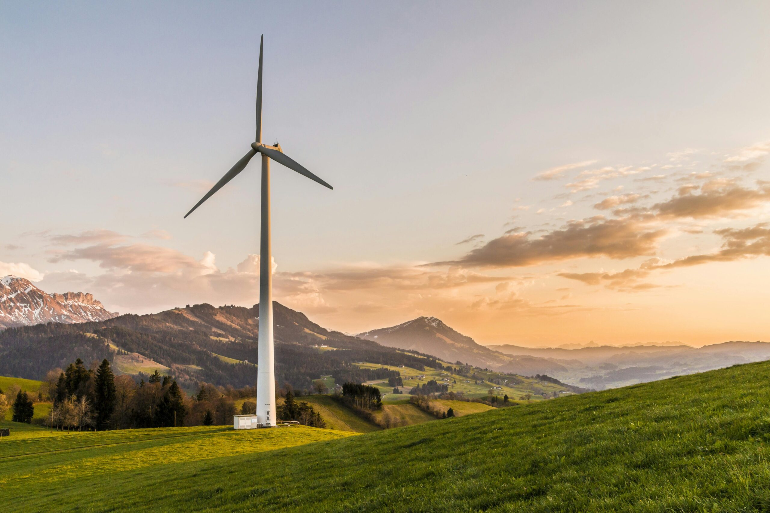 Home Wind turbine amid rolling hills and mountains at sunset, symbolizing renewable energy and sustainability.